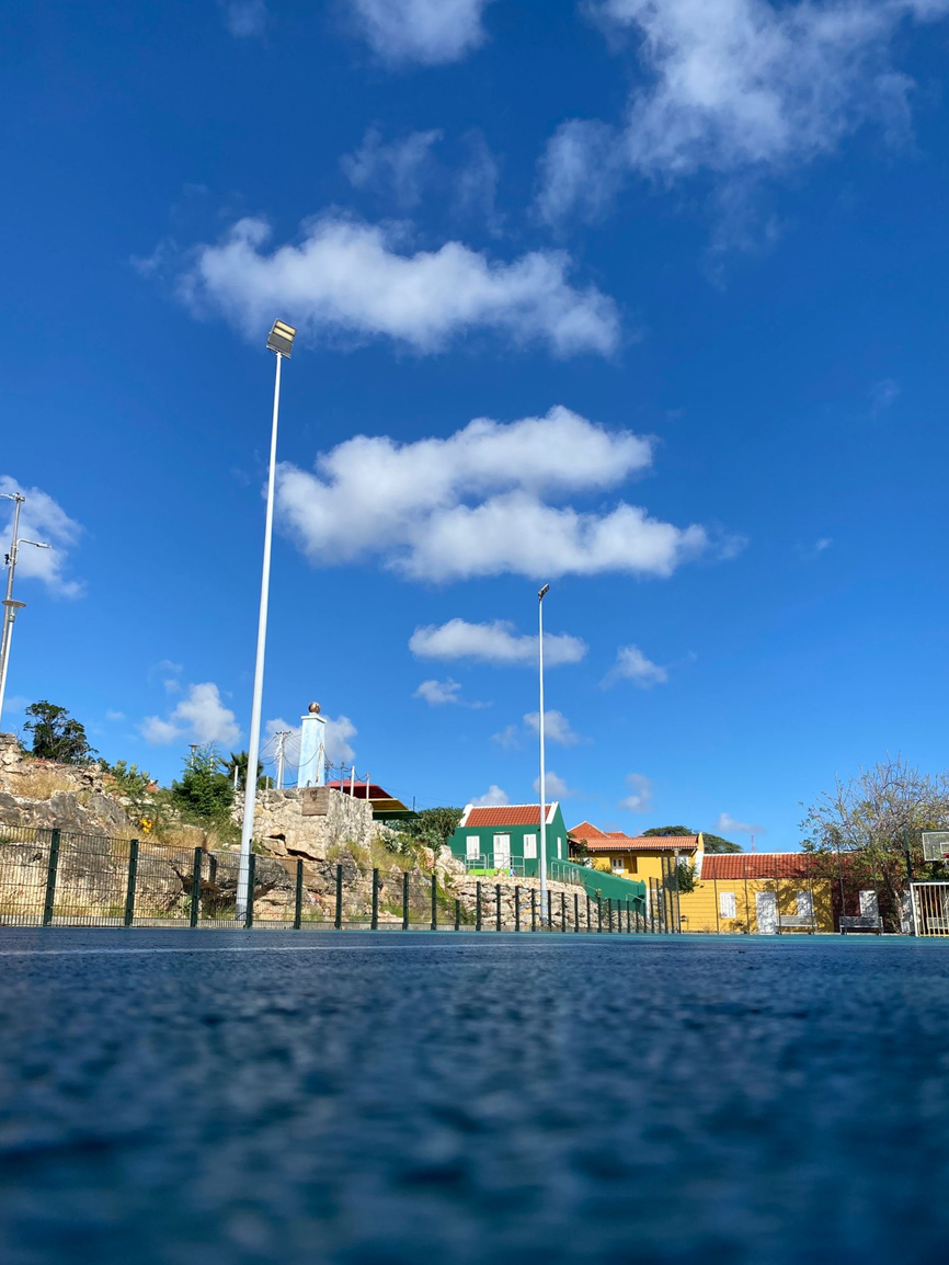 Sportveld in de bario met lichtmasten en kleurrijke huisjes — foto gemaakt door een jongere tijdens de workshop