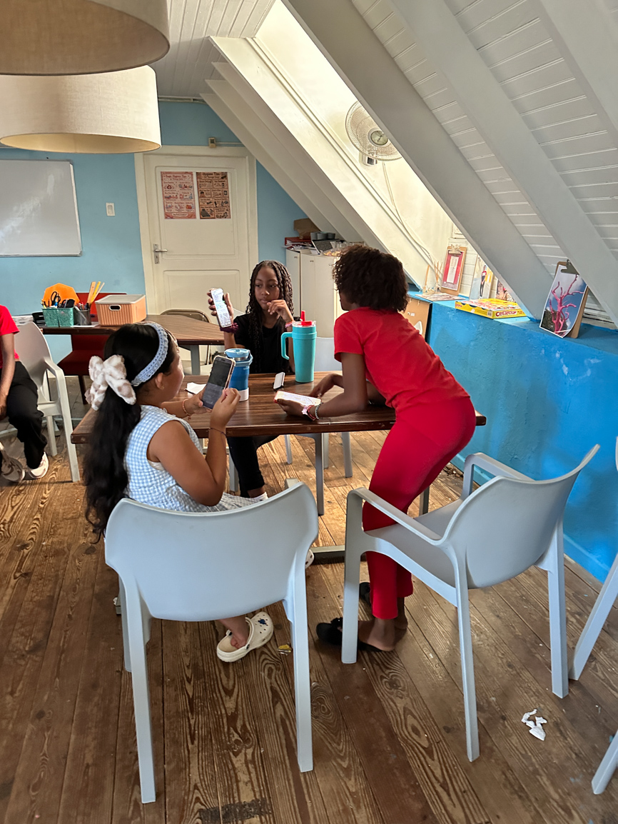 Jongeren zitten rond een tafel in het atelier en bekijken elkaars foto's