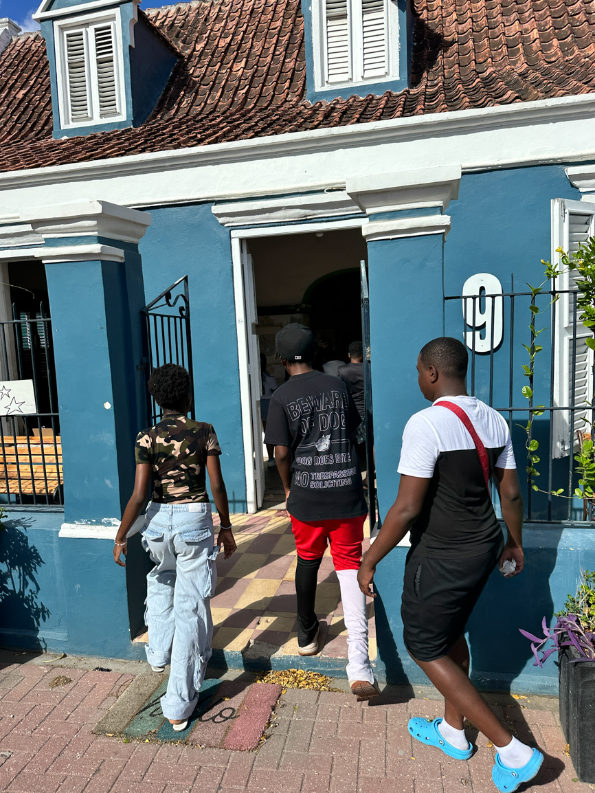 Jongeren lopen een blauw huis in Otrobanda binnen tijdens een excursie